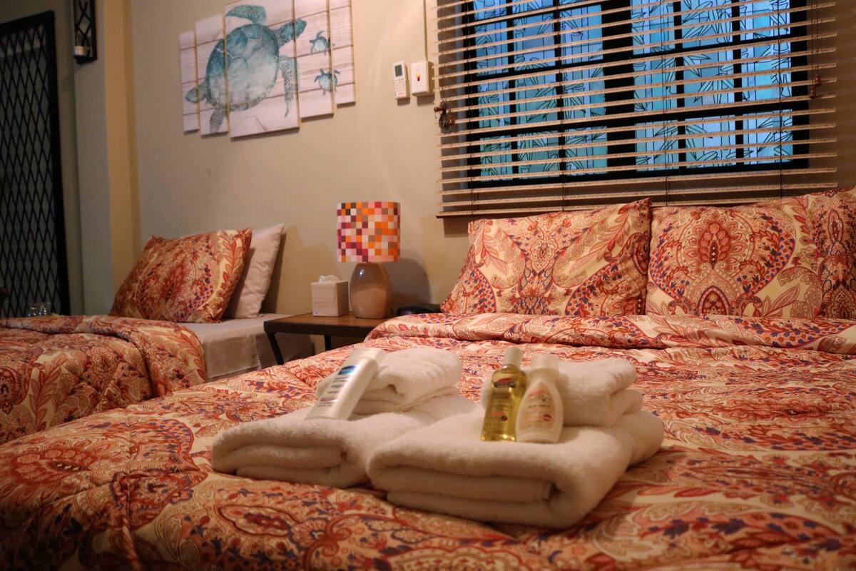 A hotel room with a bed, two pillows, a nightstand, a lamp, and a window with blinds.