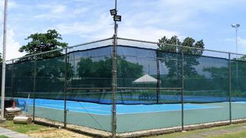 A fenced tennis court with a net, surrounded by a chain-link fence and a street lamp.