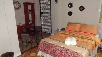 A bedroom with a bed, a desk, a chair, a small table, and a wall clock.
