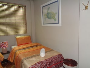 Una camera da letto con un letto, una finestra con persiane, un quadro appeso al muro e un comodino con una lampada.