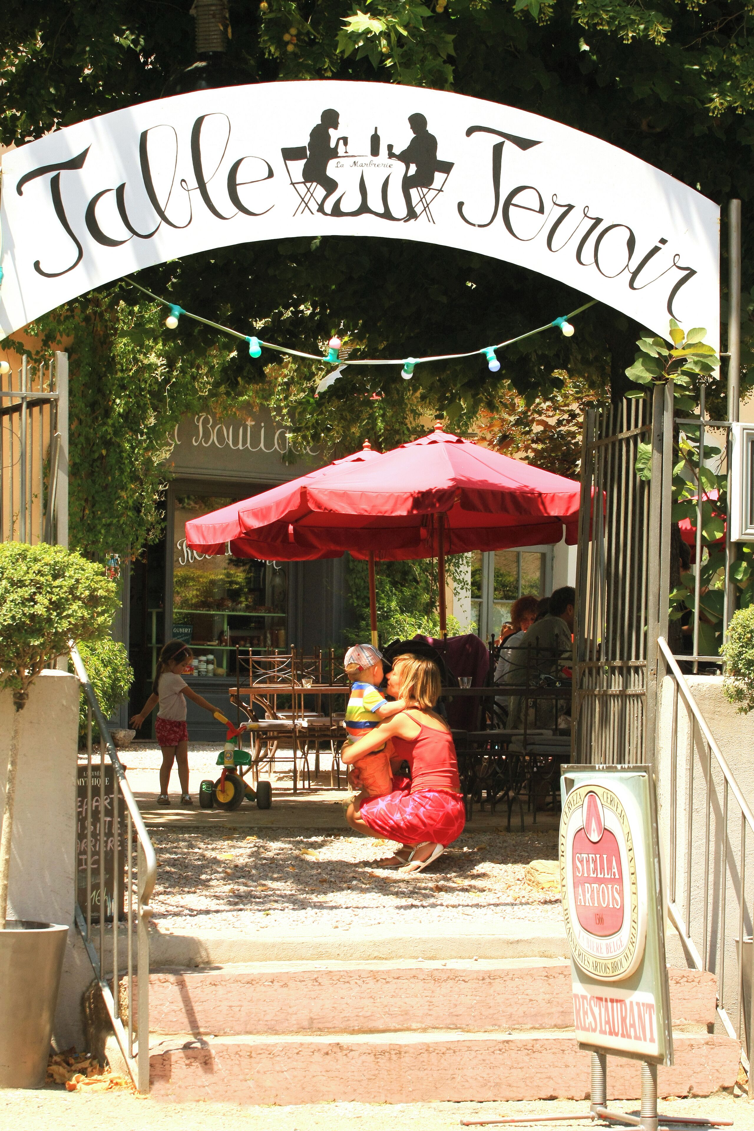 Zona d'estar a l'aire lliure amb un parasol vermell i un cartell que diu "Table Jeroir".