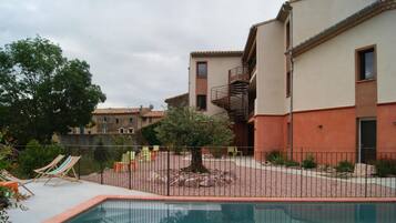 Zona de piscina con deck cercado, sillas de descanso y un árbol.