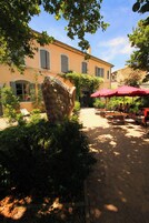 A courtyard with outdoor seating, a large stone sculpture, and a building with shutters.