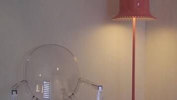 A clear plastic chair and a red floor lamp against a plain wall.
