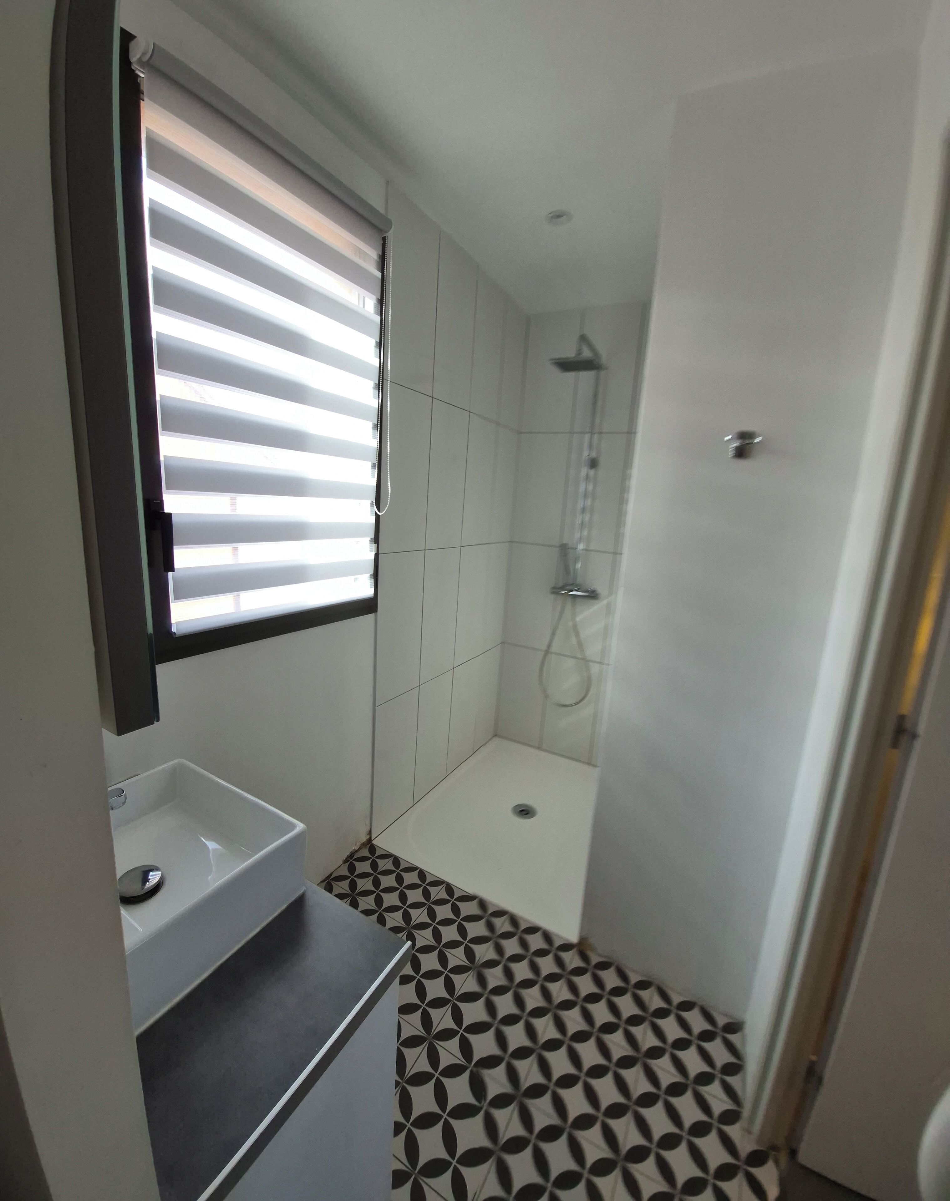 Un baño con ducha, lavamanos y una ventana con persianas.