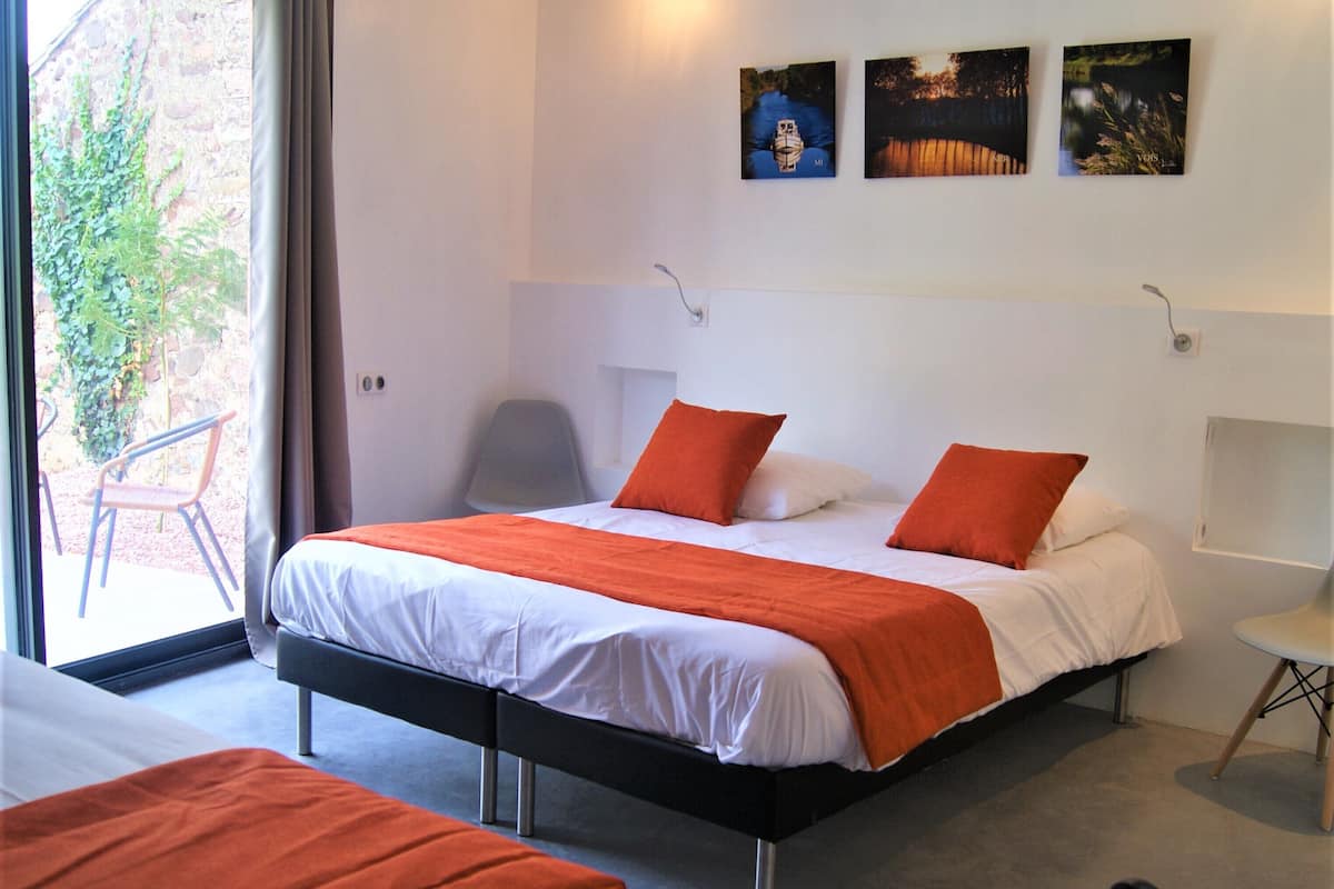 Een moderne slaapkamer met een groot bed, twee oranje kussens, een grijze stoel en een klein tafeltje.