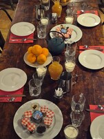 Una mesa de comedor dispuesta con platos, cubiertos, vasos, una tetera y una jarra de jugo de naranja.