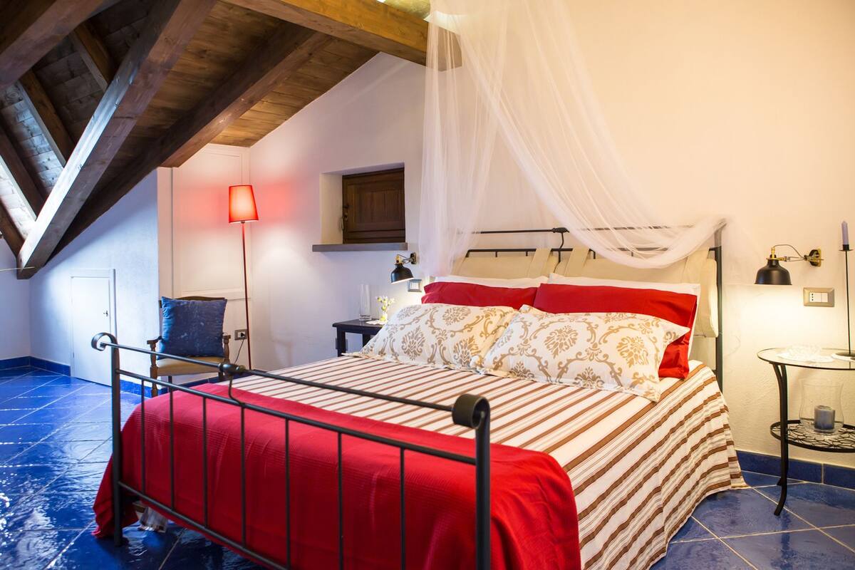 Un dormitorio con una cama, una mesita de noche, una silla, una lámpara y una ventana.