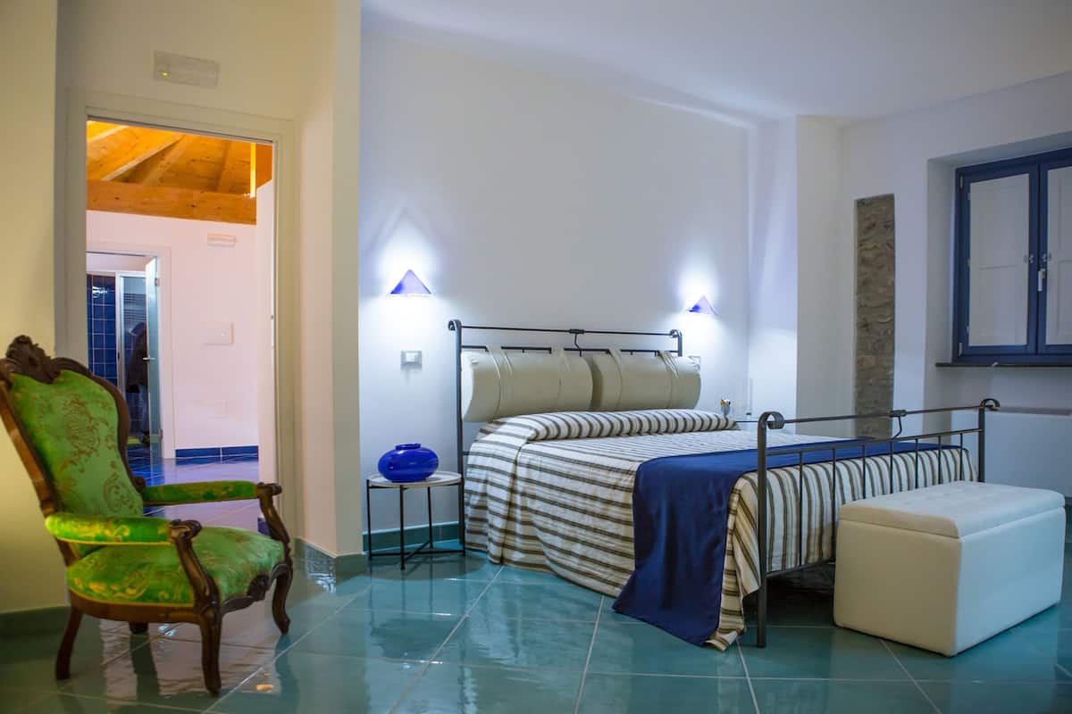 Un dormitorio con cama, una silla, mesita de noche y televisión montada en la pared.