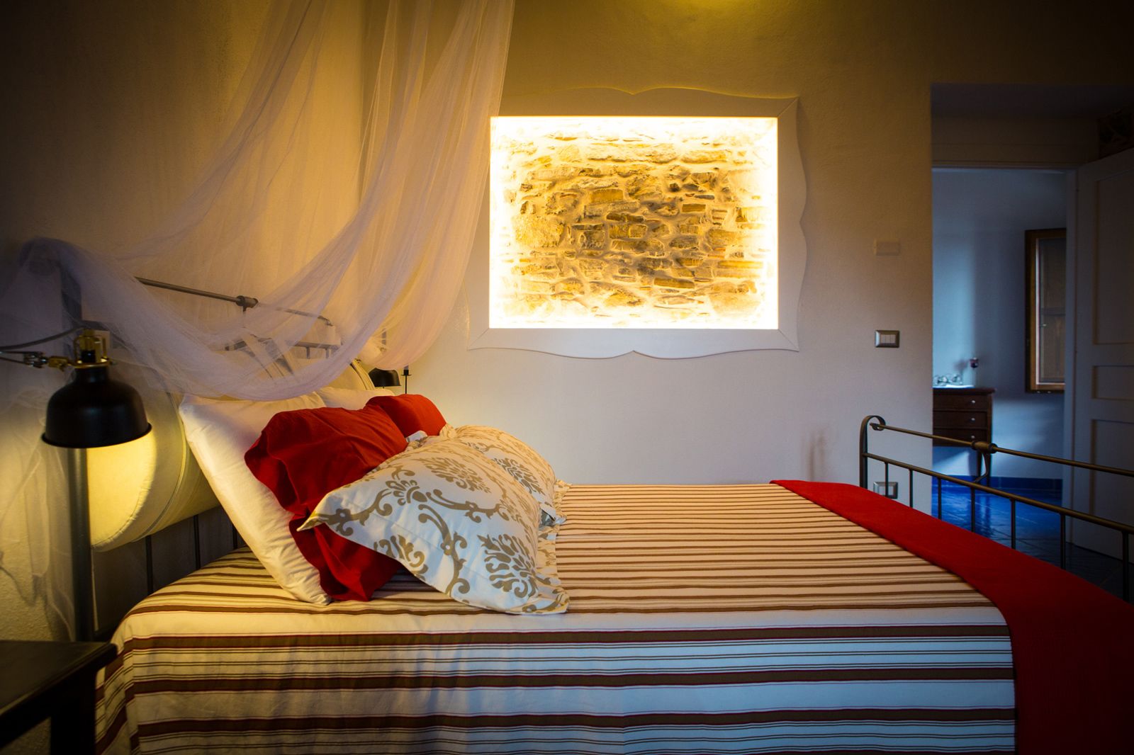 Um quarto com cama, luminária de cabeceira, janela com vista e mesa de cabeceira.