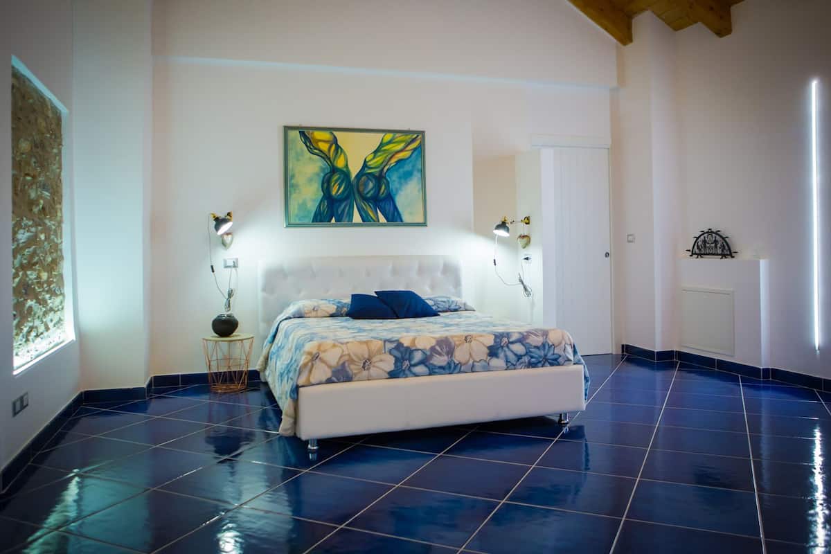 Un dormitorio con una cama grande, un cuadro sobre la cama y suelo de baldosas.