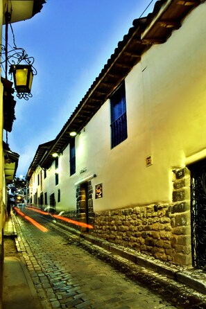 A narrow cobblestone street lined with white buildings, stone walls, and hanging lanterns.