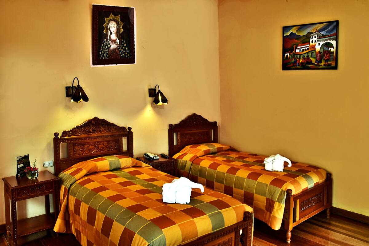 A hotel room with two wooden beds, a nightstand with a telephone and a lamp, and two wall-mounted lamps.