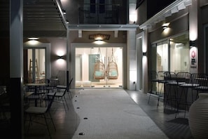 An outdoor seating area with chairs and tables, a storefront with hanging chairs, and a staircase leading to an upper level.