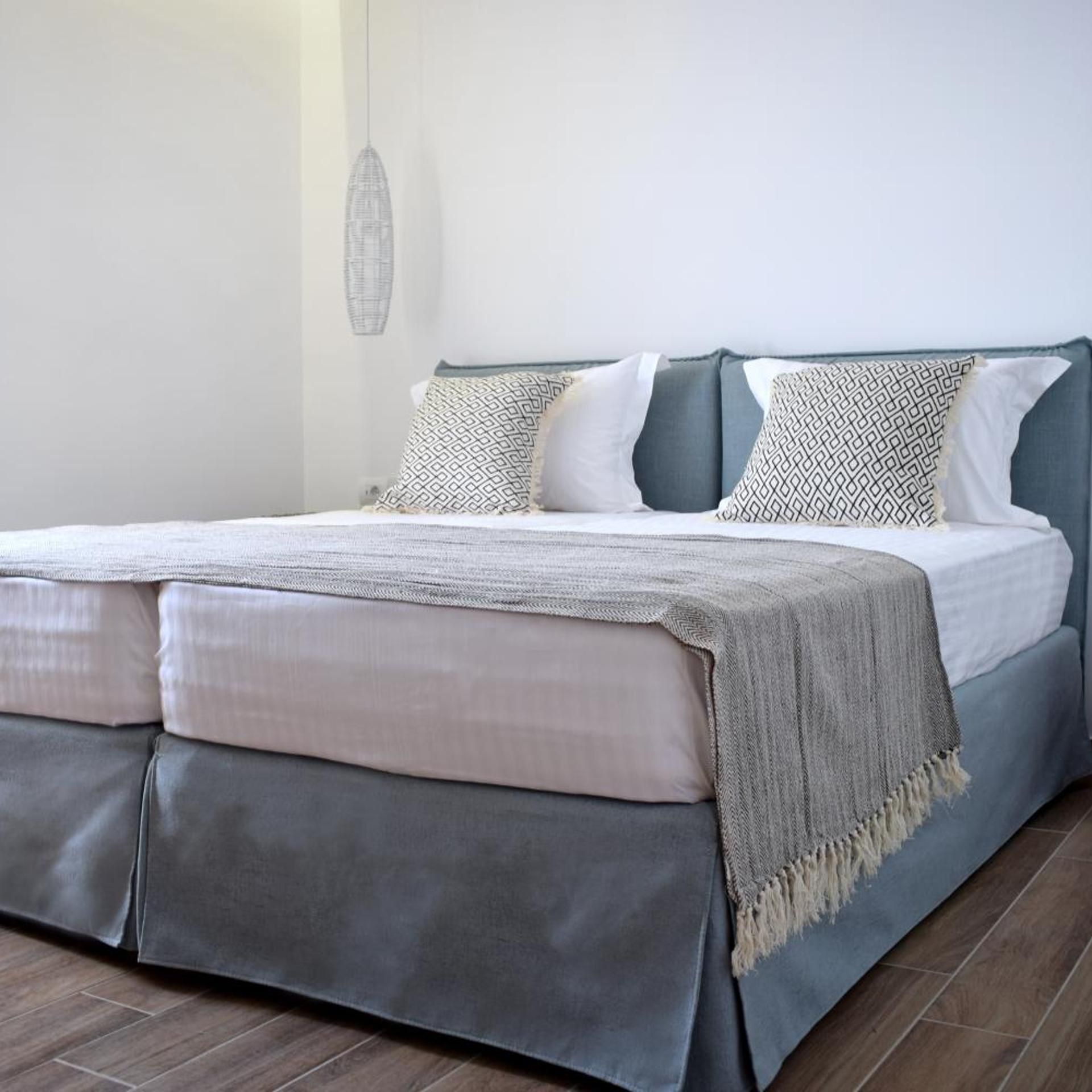 A bed with a grey headboard, white and patterned pillows, and a grey blanket.