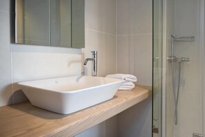 A modern bathroom with a white vessel sink, a mirror above it, and a glass-enclosed shower area.