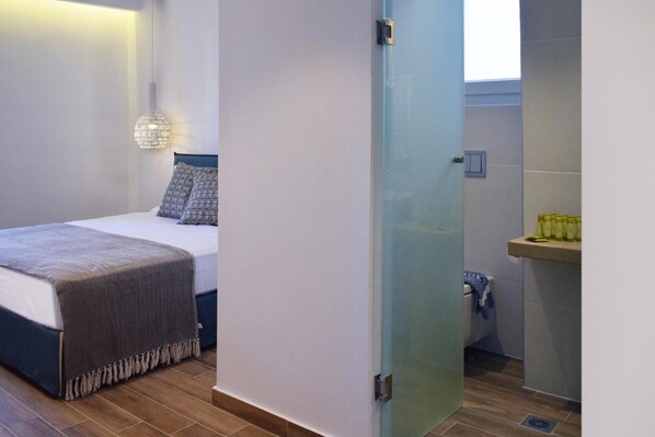 A bedroom with a bed, bedside lamp, and a bathroom with a sink and toiletries.