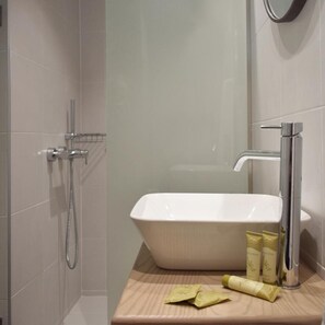 A bathroom with a white sink, a handheld showerhead, and toiletries on the countertop. - Meltemi Hotel (Skiathos)