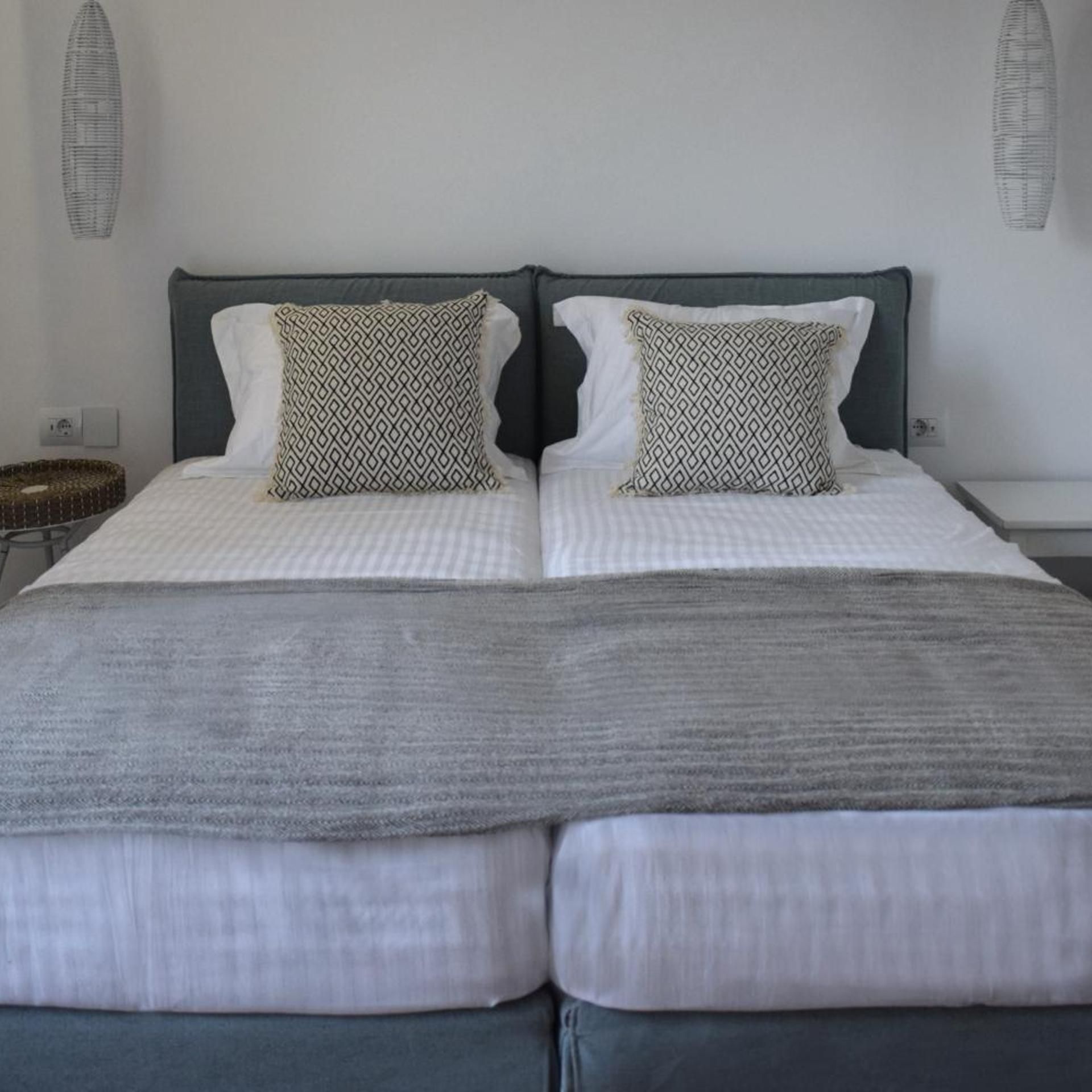 Un lit double avec une couverture grise, deux coussins à motifs et une tête de lit grise.