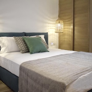 A neatly made bed with a white duvet, a blue headboard, and two pillows, one green and one patterned.
