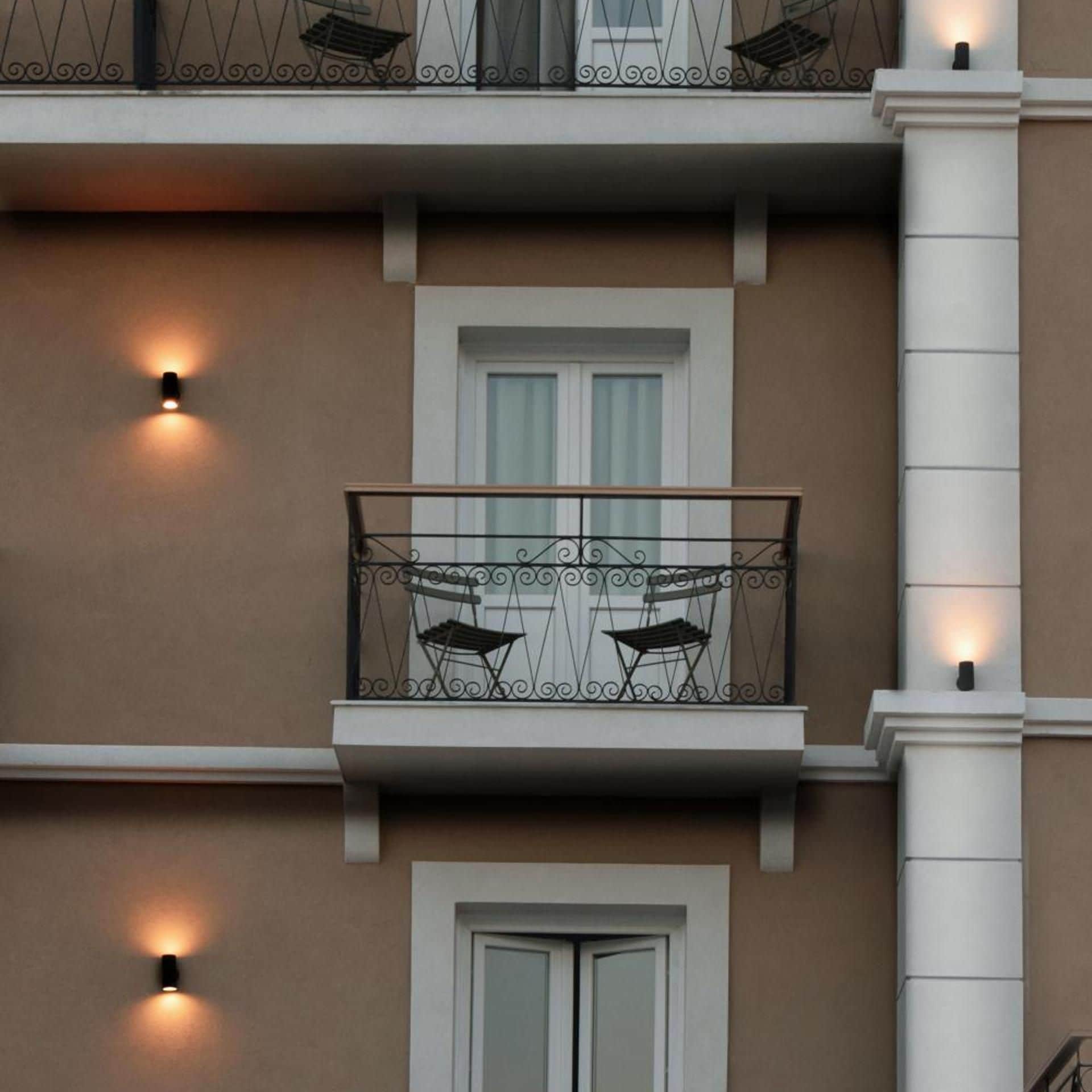 A building facade with a balcony, two doors, and two wall-mounted lights.