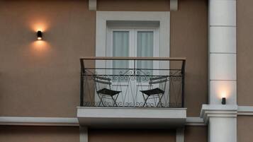 A building facade with a balcony, two doors, and two wall-mounted lights.