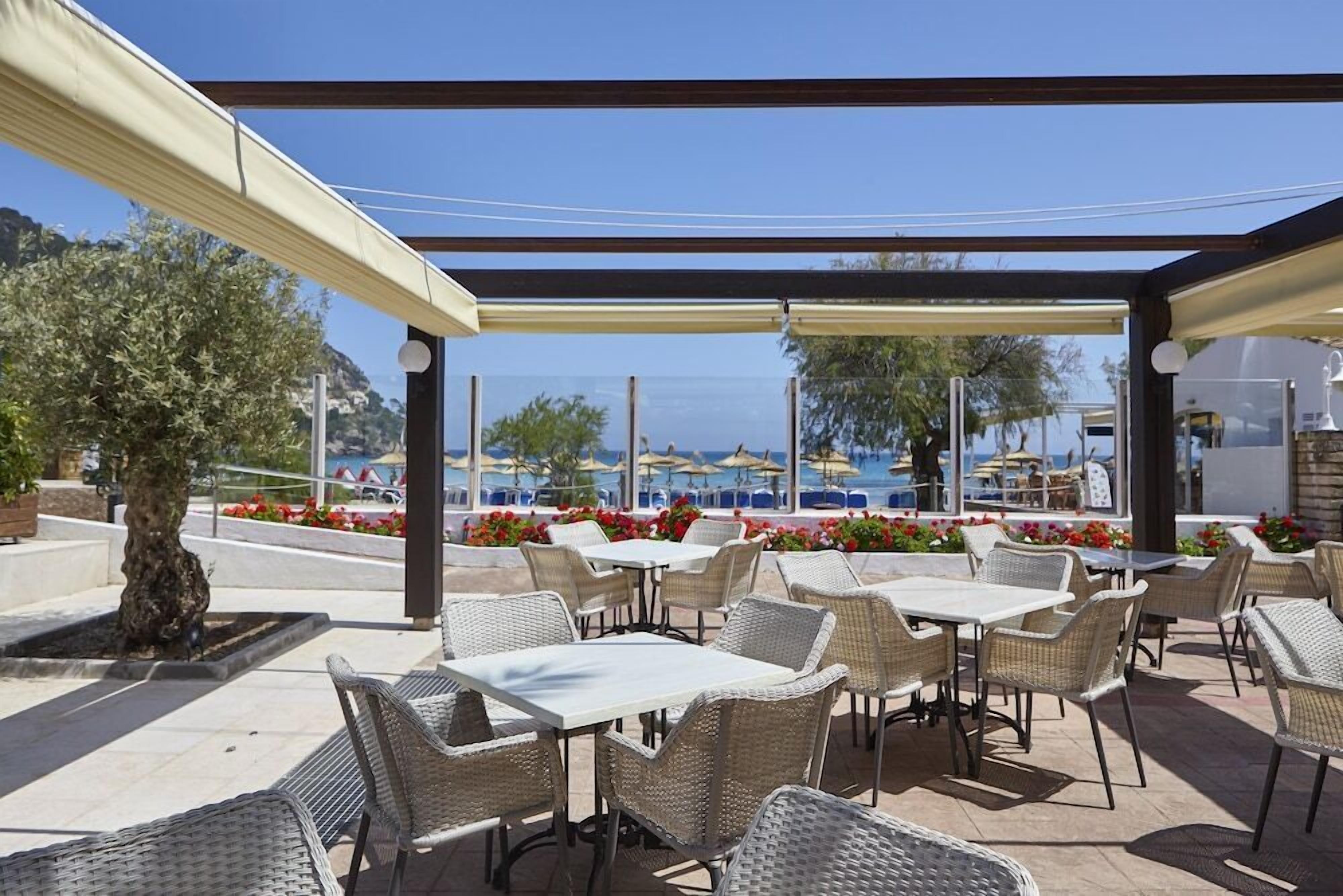 Un patio al aire libre con mesas y sillas de mimbre, un espacio de estar cubierto y vista al mar.