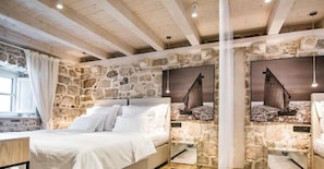 A bedroom with a stone wall, a bed, a window with curtains, and a painting of a sailboat. - Apartmani Orlando (Dubrovnik)