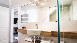 A modern bathroom with a large mirror, a white sink, and a glass shower enclosure. - Apartmani Orlando (Dubrovnik)