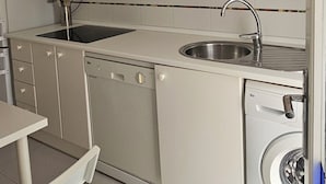 Una cuina compacta amb armaris blancs, una barra, un rentaplats i una rentadora.