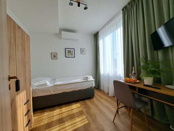 Ein modernes Hotelzimmer mit einem Bett, einem Schreibtisch mit Stuhl, einem Fernseher und einem Fenster mit Vorhängen.