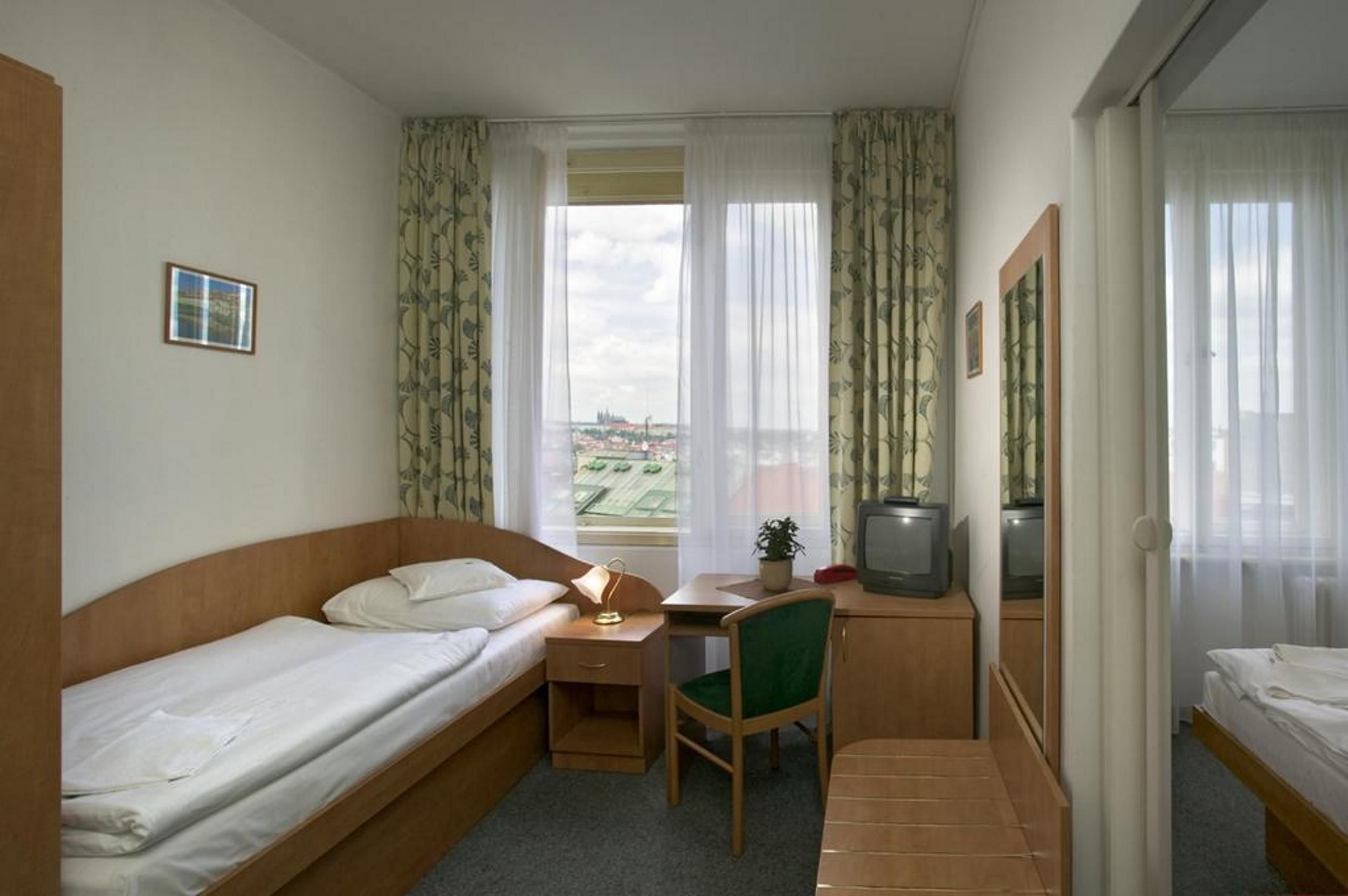 Una habitación de hotel compacta con dos camas individuales, un escritorio con silla, televisión y ventana con cortinas.