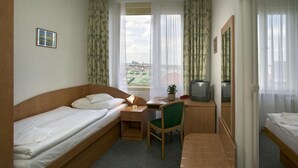 Camera d'albergo compatta con due letti singoli, una scrivania con sedia, televisione e finestra con tende.