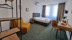 Ein Hotelzimmer mit einem Bett, einem Schreibtisch mit Stuhl, einer Couch, einem Hängesessel und einem kleinen Tisch mit Flasche und Gläsern.