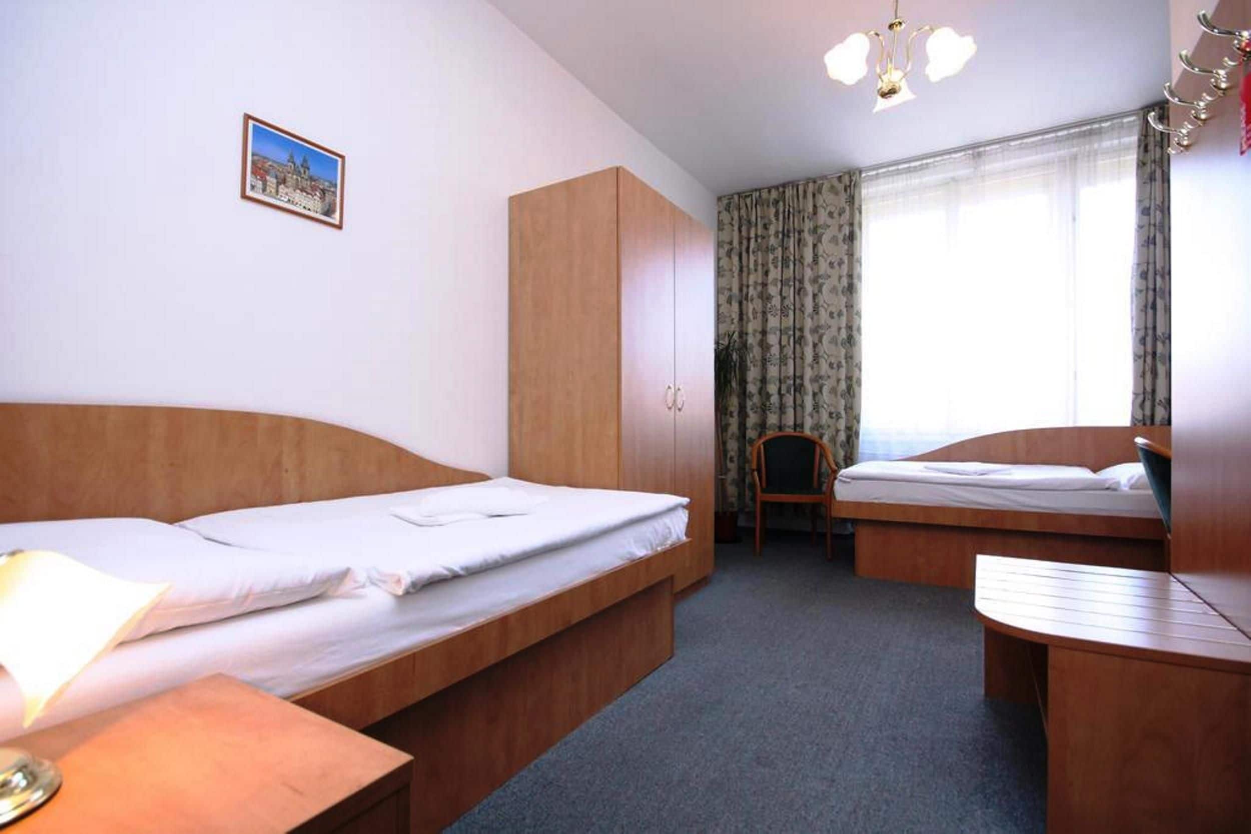 Quarto de hotel com duas camas, um guarda-roupa de madeira, uma cadeira e uma mesinha.
