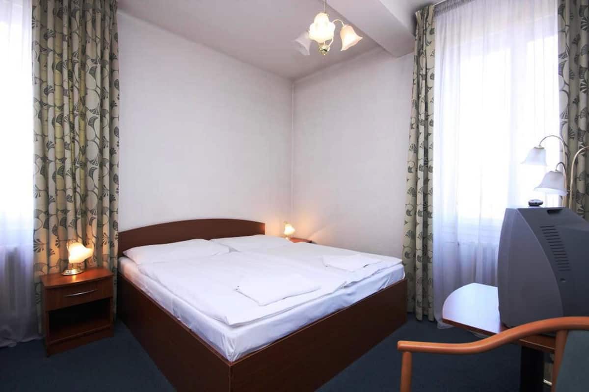 A hotel room with a single bed, bedside tables with lamps, a desk with a chair, and a television.