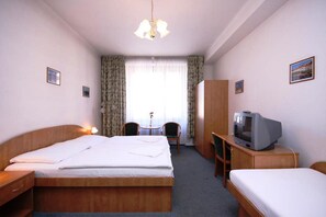 A hotel room with a single bed, a desk with a television, a chair, and a wardrobe. - Legie (Prague)