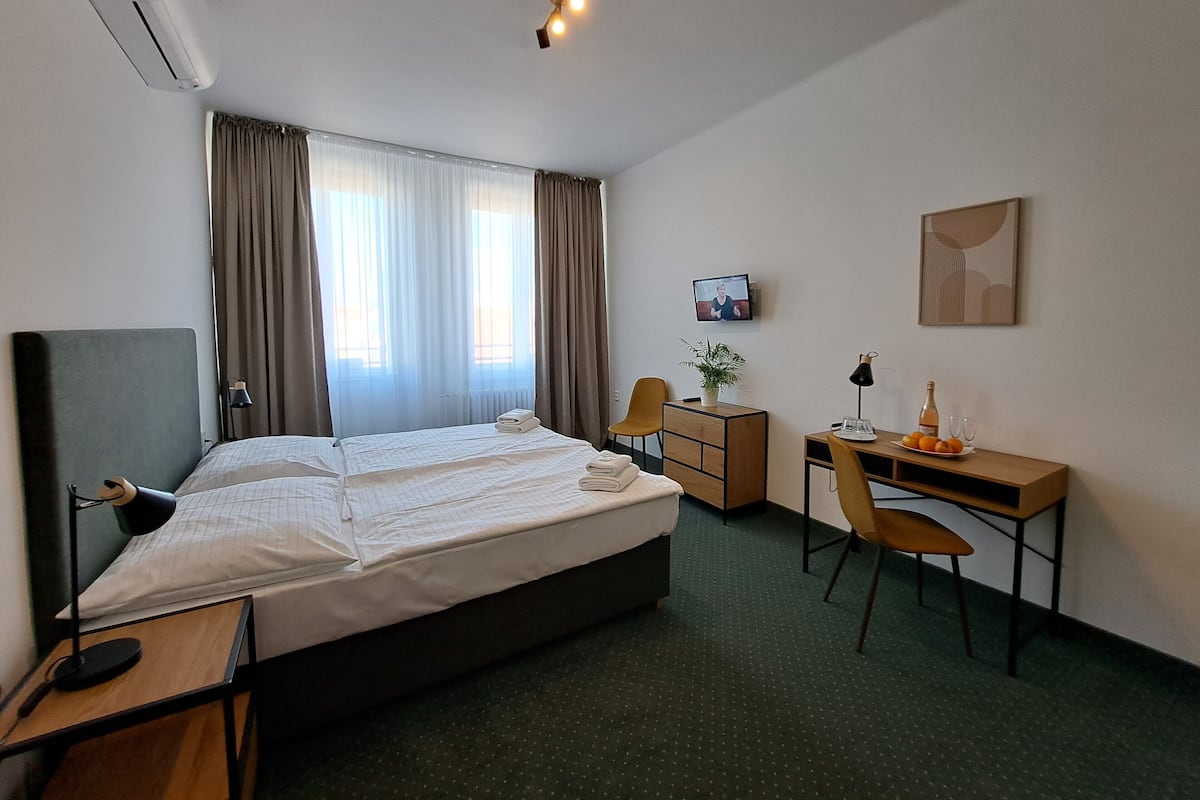 A hotel room with a bed, a desk, a chair, a TV, and a window with curtains.
