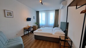 A hotel room with a bed, a desk, a chair, a television, and a window with curtains.