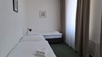 Habitación de hotel con dos camas individuales, una mesita de noche con lámpara, un cuadro en la pared y una ventana con cortinas.