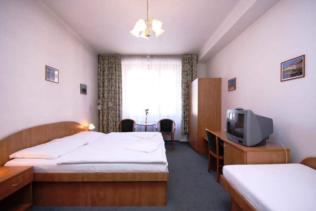 A hotel room with a single bed, a desk with a television, a chair, and a wardrobe.