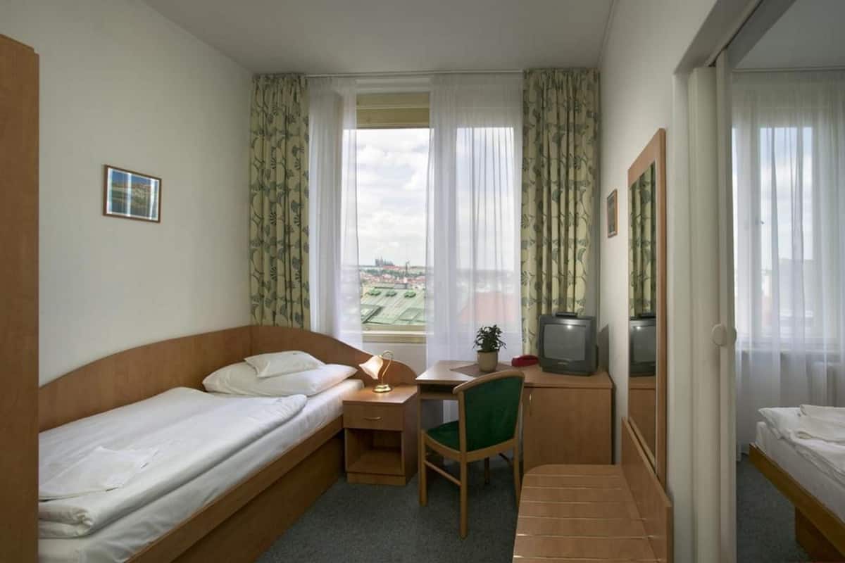 A compact hotel room with two single beds, a desk with a chair, a television, and a window with curtains.