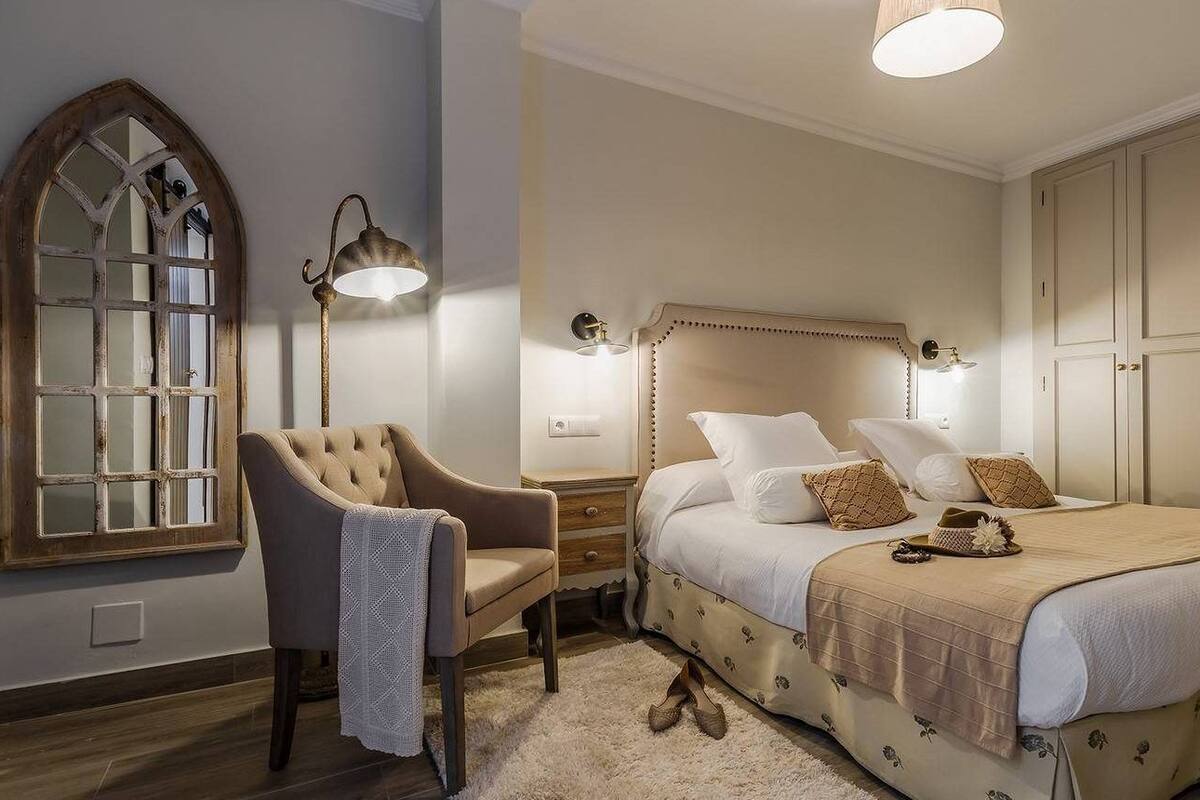 A bedroom with a large bed, a chair, a wardrobe, and a mirror.
