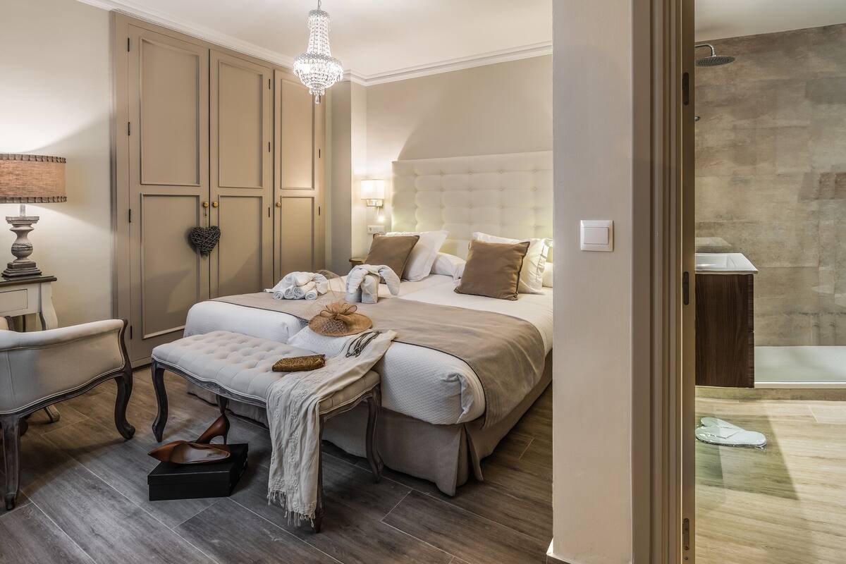 A bedroom with a large bed, a bench, a dresser, and a chandelier.