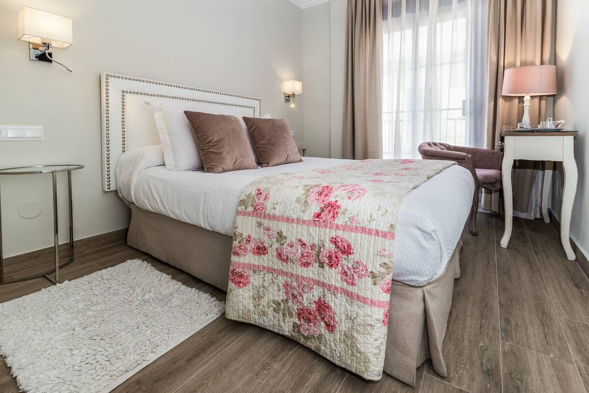 A neatly arranged bedroom with a bed, bedside lamps, a chair, and a small table.