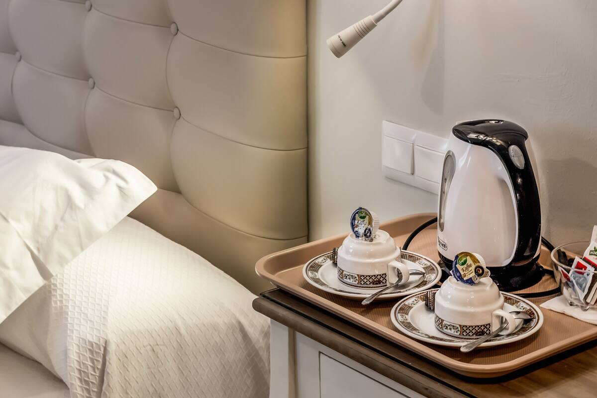 A hotel room with a bed, a bedside table with a kettle, teapot, cups, and a tray.