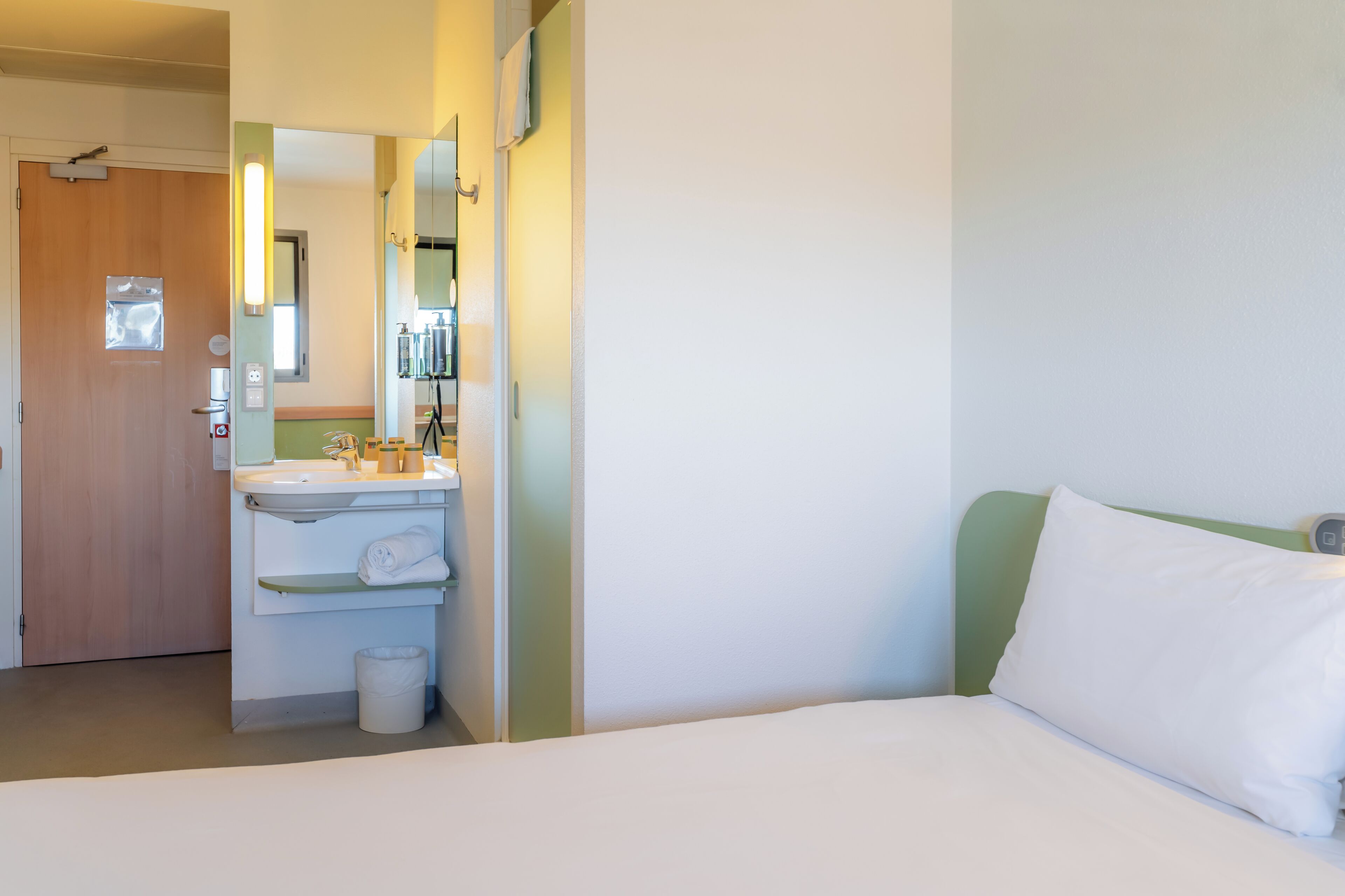 A hotel room with a bed, a bathroom with a sink, mirror, and towel rack.