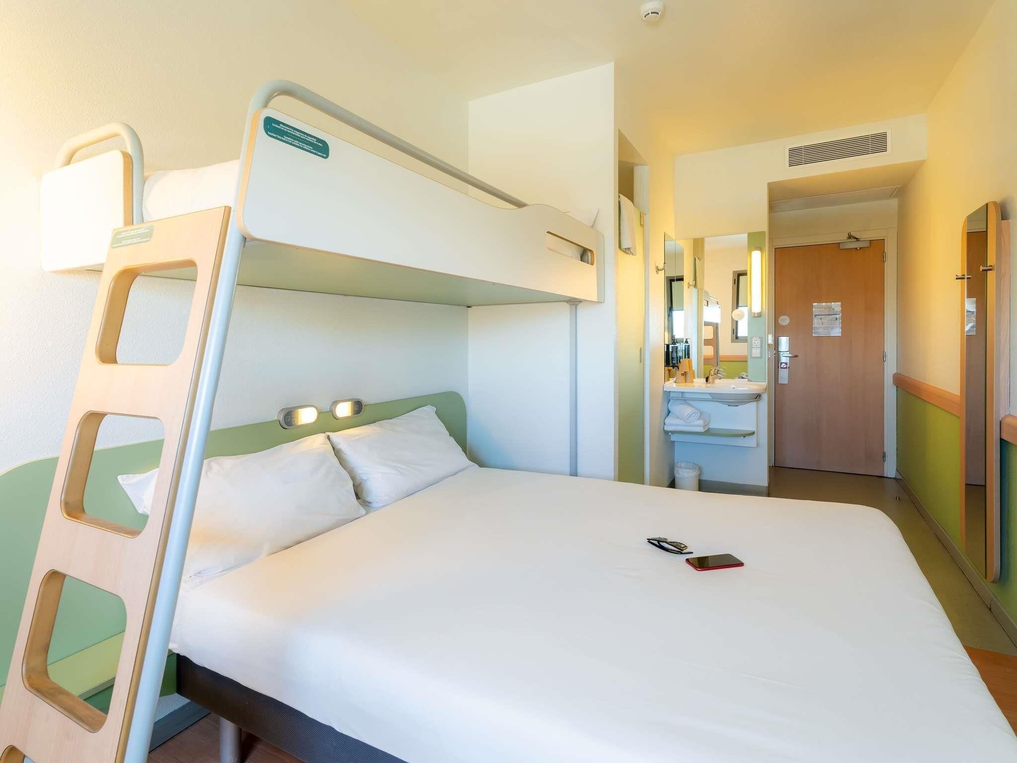 Cama litera con escalera, una mesita de noche y un espejo. Hay un baño con lavamanos y un espejo.