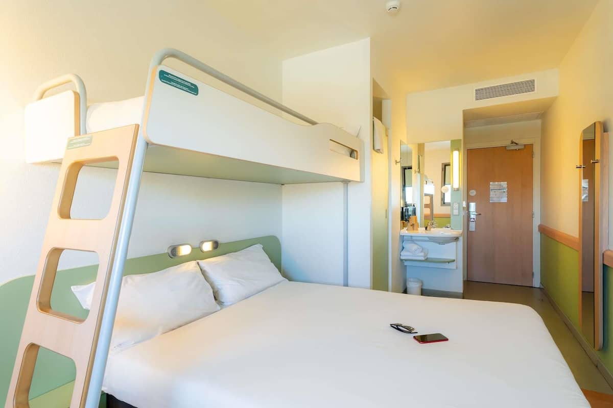Cama litera con escalera, una mesita de noche y un espejo. Hay un baño con lavamanos y un espejo.