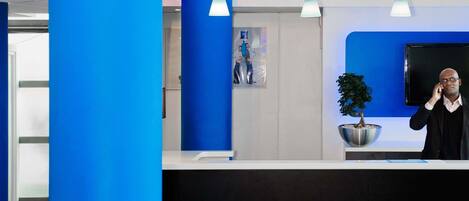A reception desk with a blue accent wall, a potted plant, and pendant lighting.